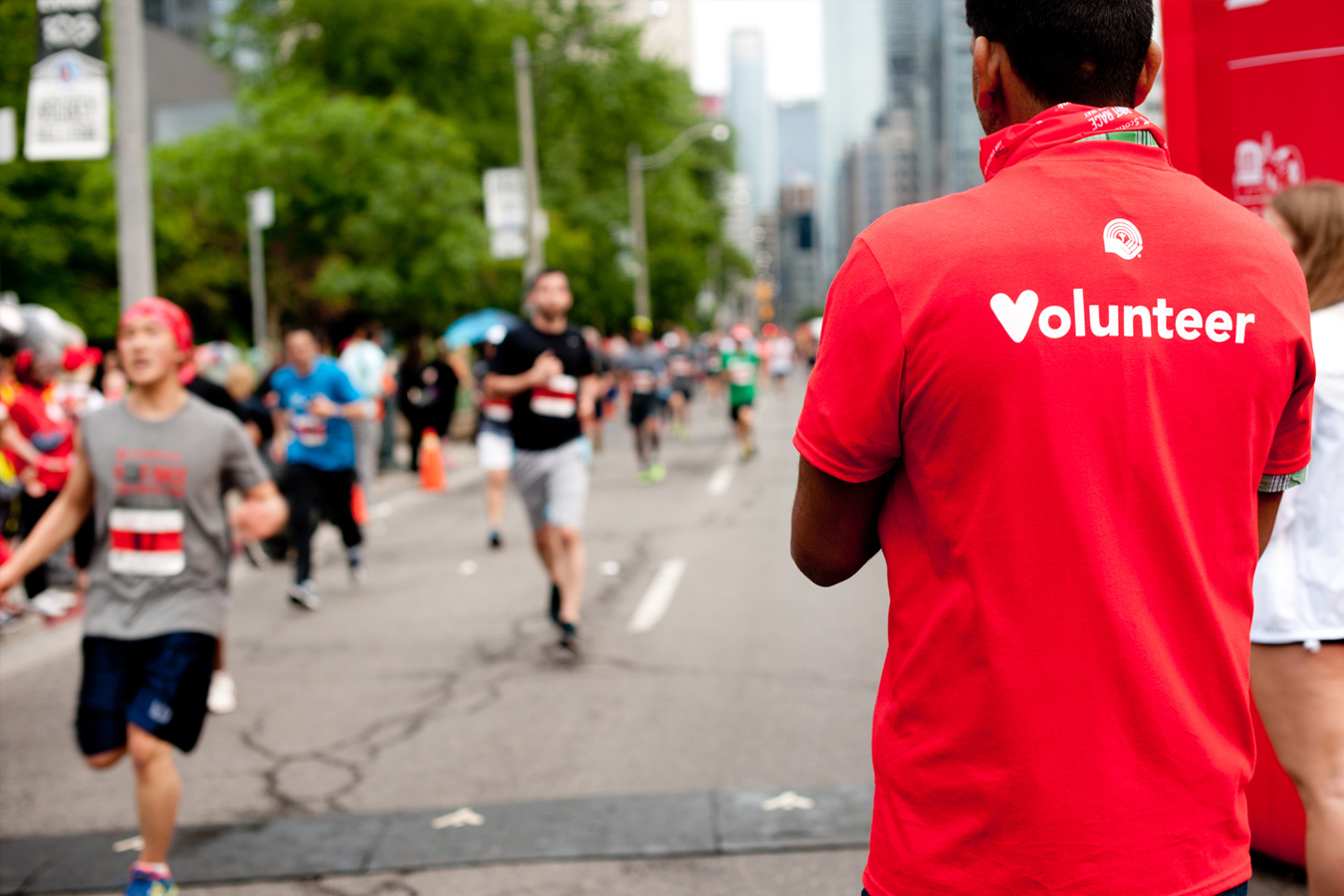 Man in red shirt reading Volunteer with people running race in background