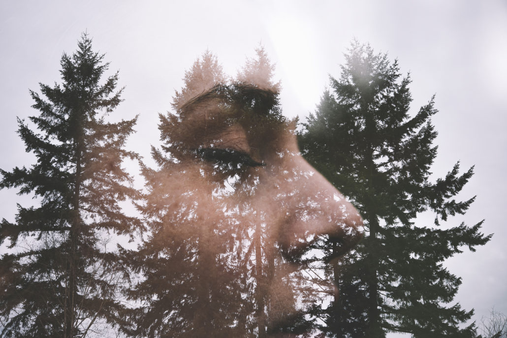 profile view of woman with eyes closed superimposed on evergreen trees and sky