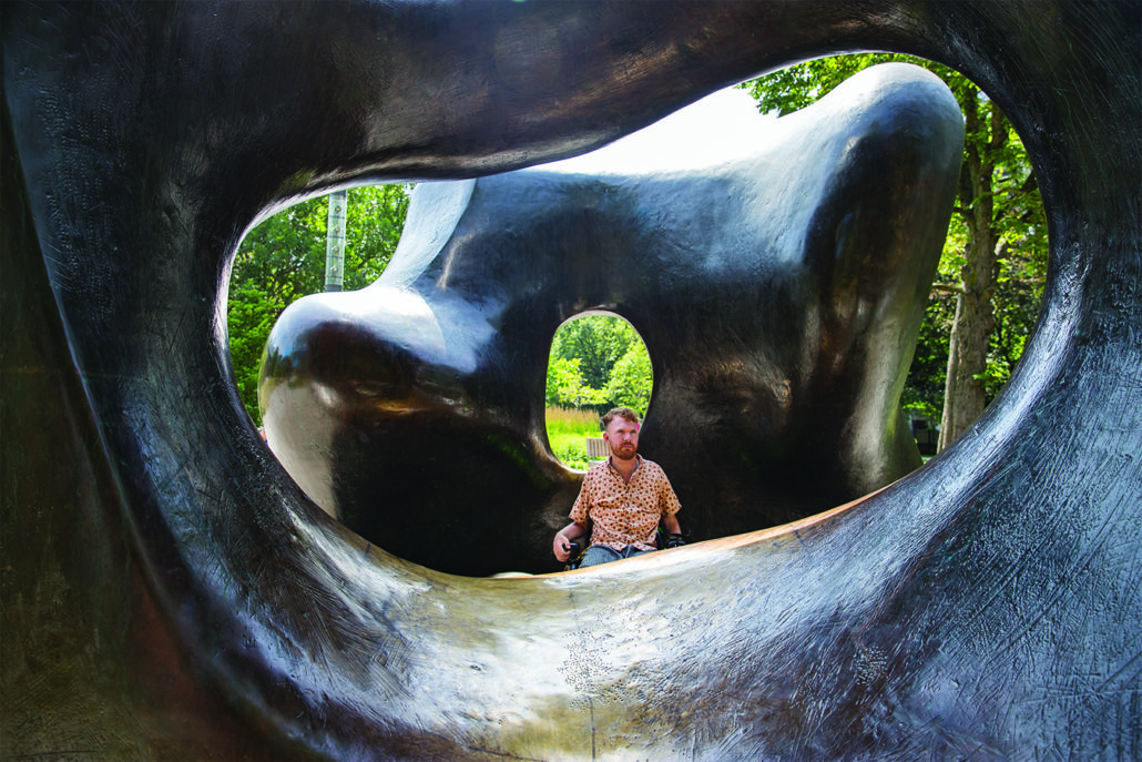 Anderson sits in his wheelchair behind a large sculpture in a public park