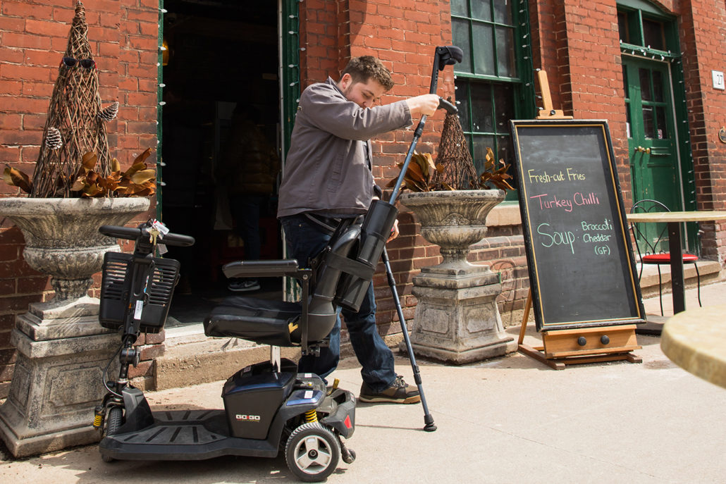 Image of a man holding crutches in front of a mobility scooter