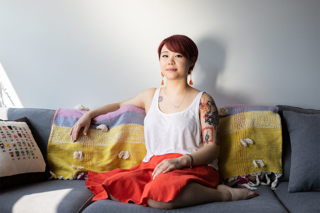 Van Loc wearing white top orange skirt seated on grey couch