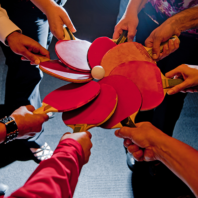 Eight people holding ping pong paddles gathering in a circle.