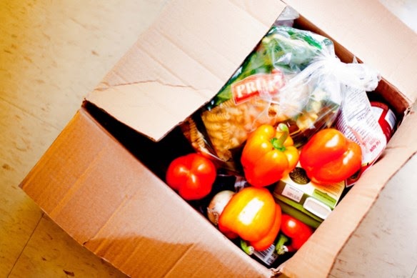 A food basket with vegetables, pasta and other groceries