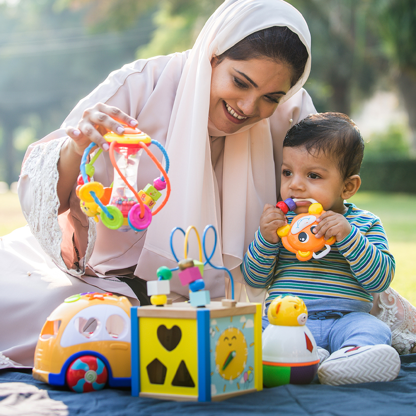 A middle eastern mom with traditional dress and young son are outdoors on a sunny day playing.