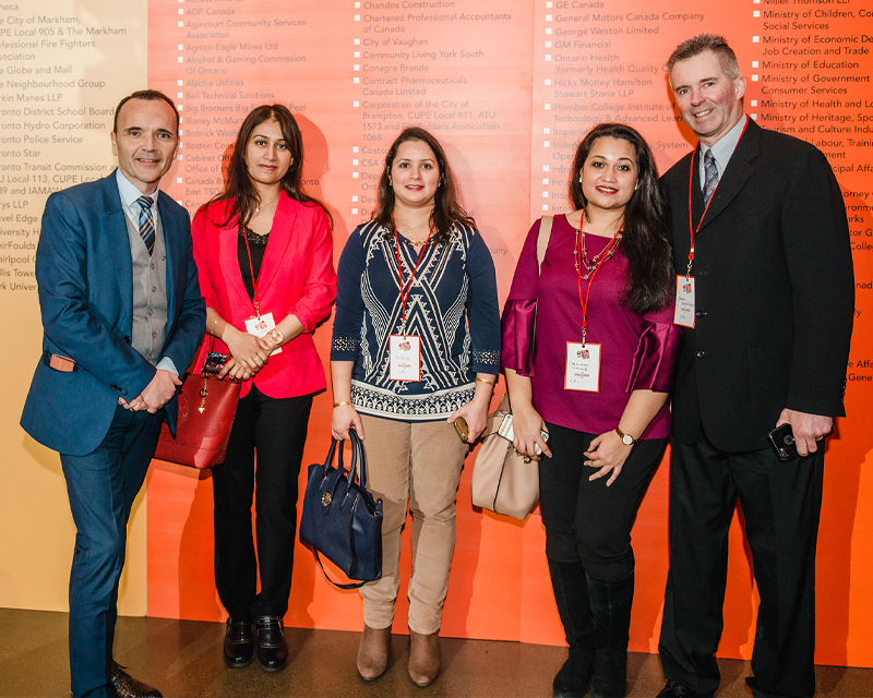 Five people standing side by side in front of a large canvas
