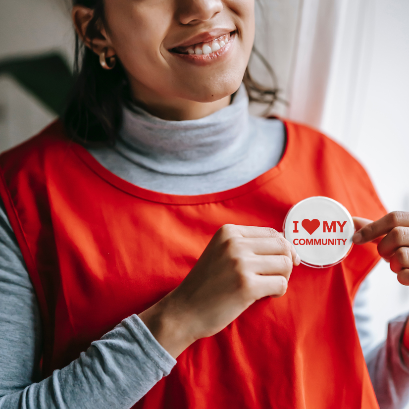 A women smiling and holding a I Love My Community button on her chest.