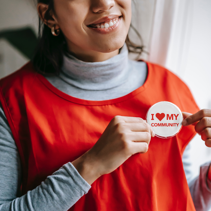 A women holding a round volunteer button smiling.