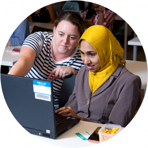 Two woman are sitting in a computer lab. The order woman is helping with a computer project.