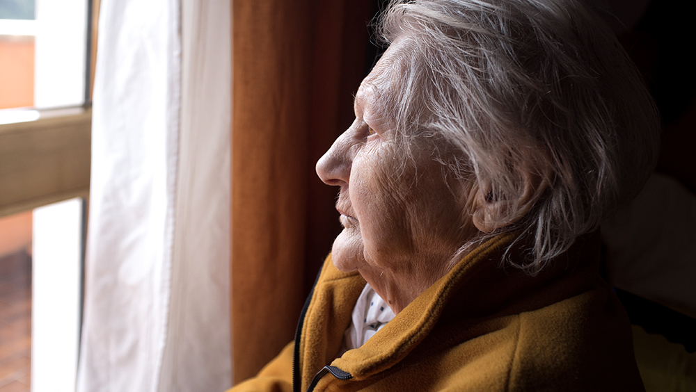 A lonely senior woman looking out window.