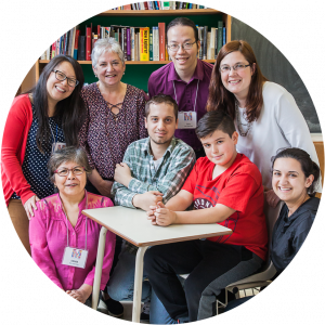 Seven education professionals surround a young boy who is sitting on a chair, all smiling