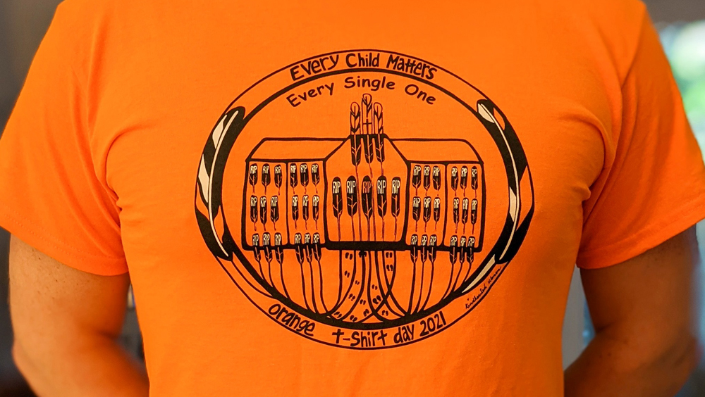 A close shot of a orange t-shirt that has graphic of unmarked graves at residential schools.