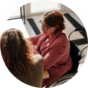 A women sitting on wheelchair having a conversation with another women indoor