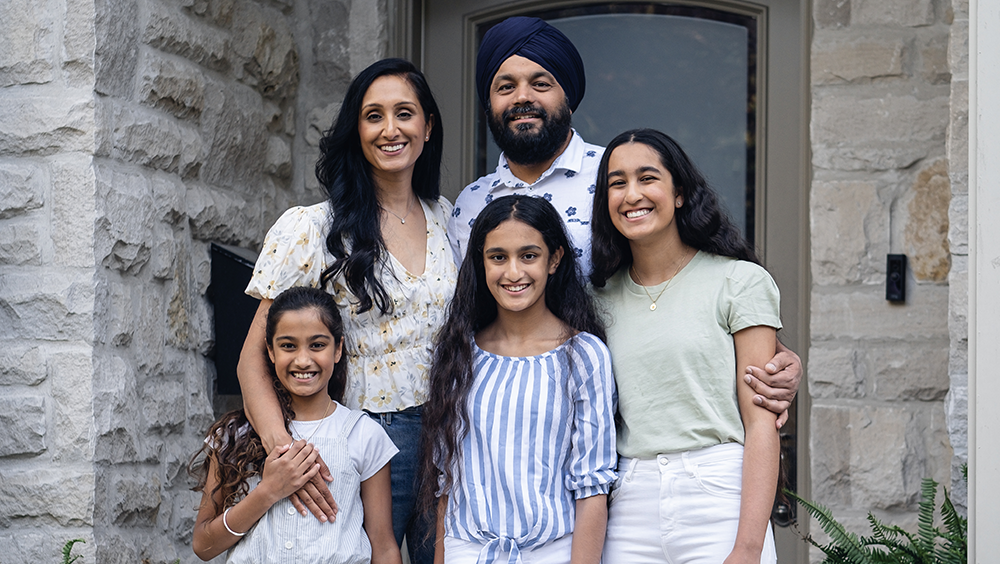 Dilprit & Rajbinder Grewal standing with their children—Simrit, Daya and Bani—in front of their home, looking at the camera.
