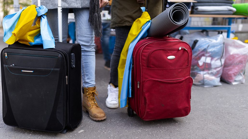 Photo of two people standing with suitcases with blue and yellow ribbons tied to them