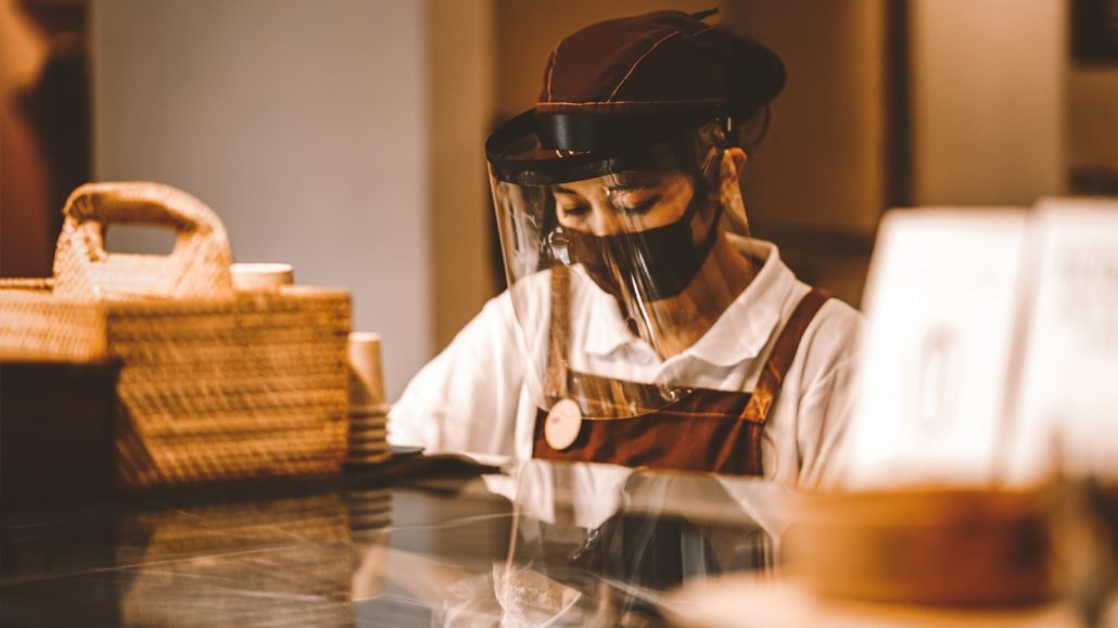 A barista wearing PPE works behind a counter.