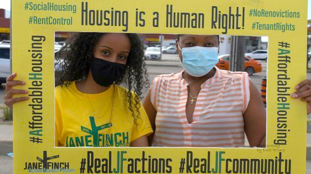 Photo of two people wearing masks holding up a frame that says “Housing is a human right!”