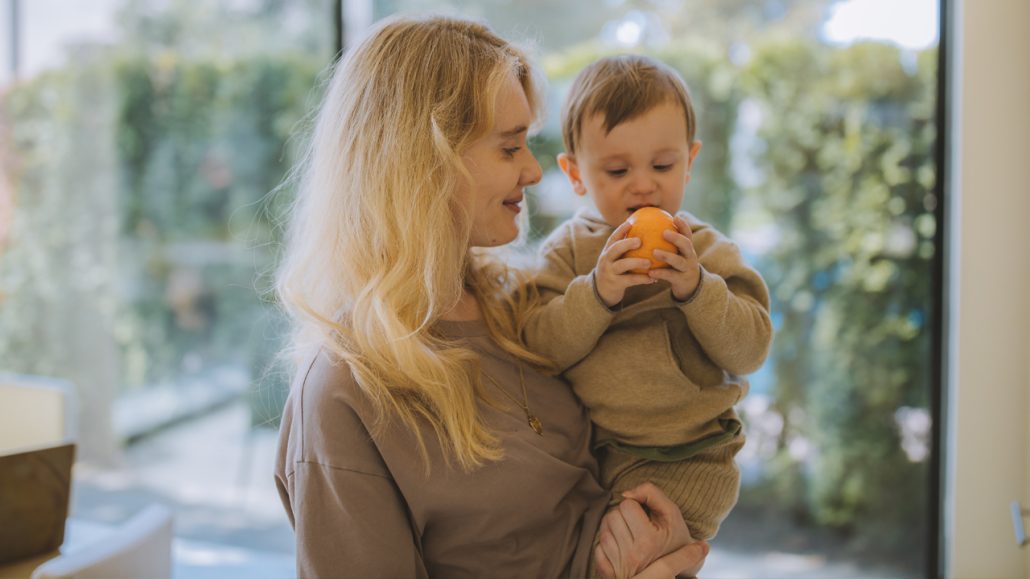 A mother holds her baby who is playing with an orange