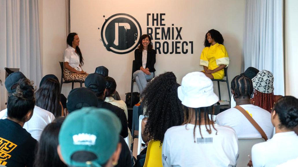 Photo of three speakers sitting in front of an audience at a Remix Project event