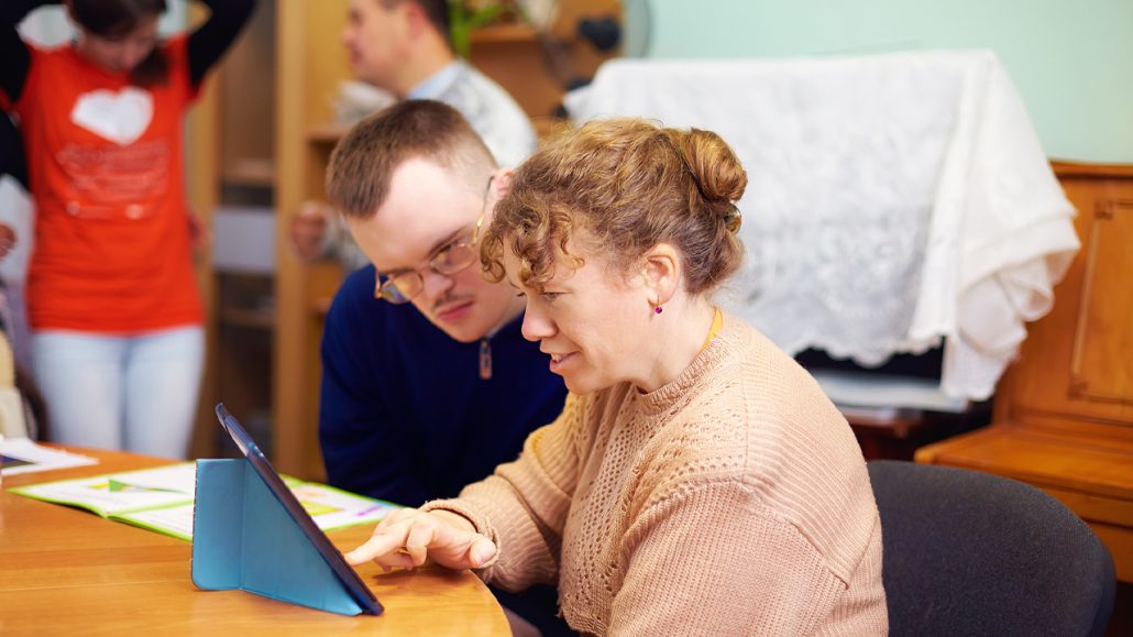 Two people, one of whom has a disability, look at an iPad together.