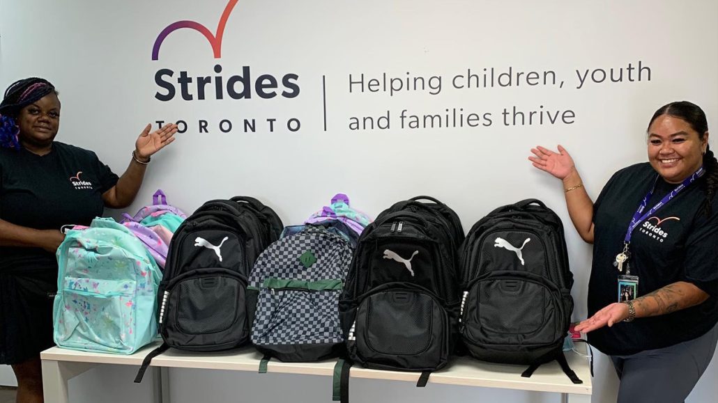 Two Strides Toronto staff members stand with a pile of backpacks