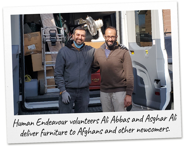 Two Human Endeavour volunteers pose in front of a van filled with furniture they’re out to deliver