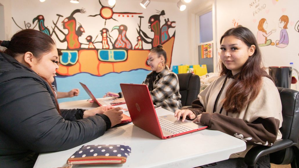 As part of ENAGB Indigenous Youth Agency programming, young people sit at a table with laptops having a discussion. 