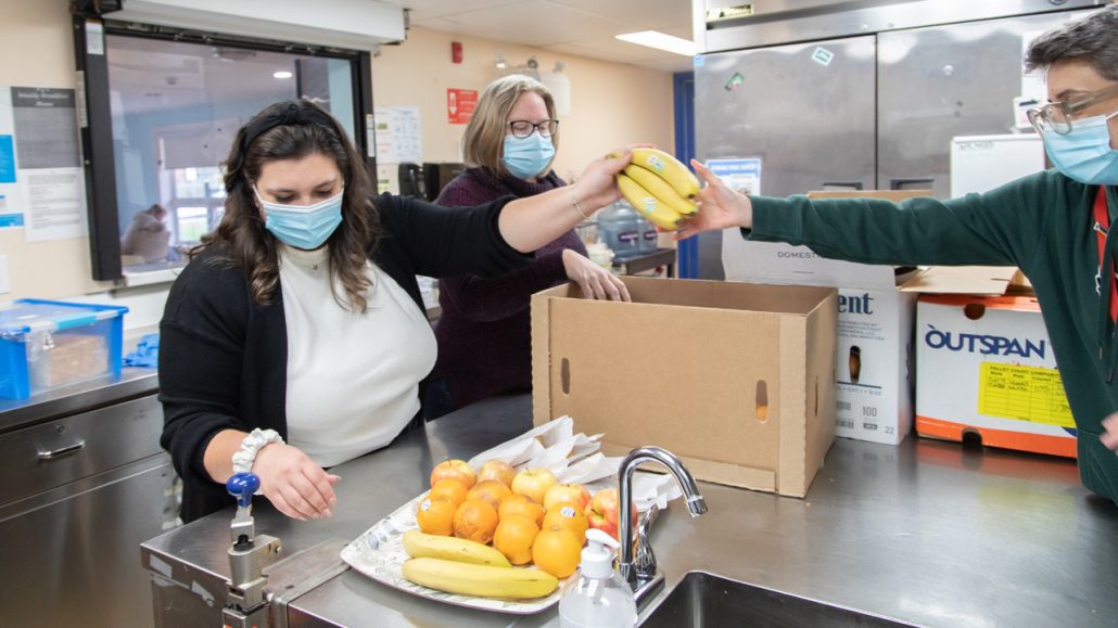 Three Blue Door volunteers unpack fresh fruit.