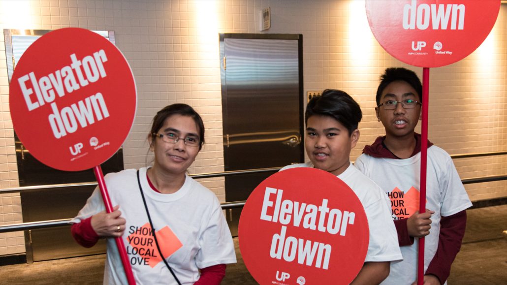 Three volunteers directing people where to go and holding signs that say ‘Elevator Down.’