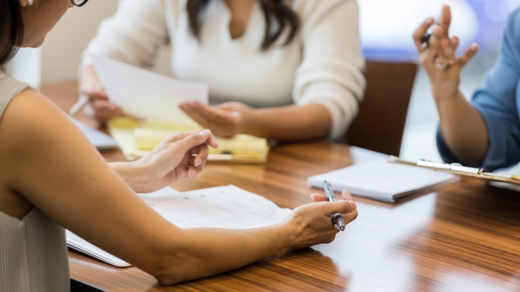 Photo of three women sitting around a conference table working on a project together.