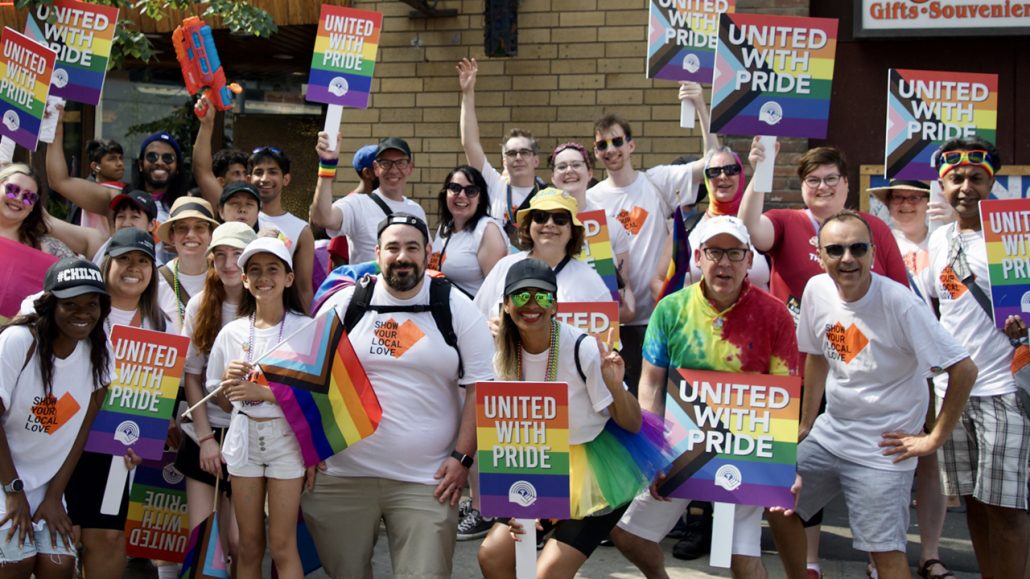 A group of United Way staff cheering and holding ‘United With Pride’ signs at the Toronto Pride Parade.