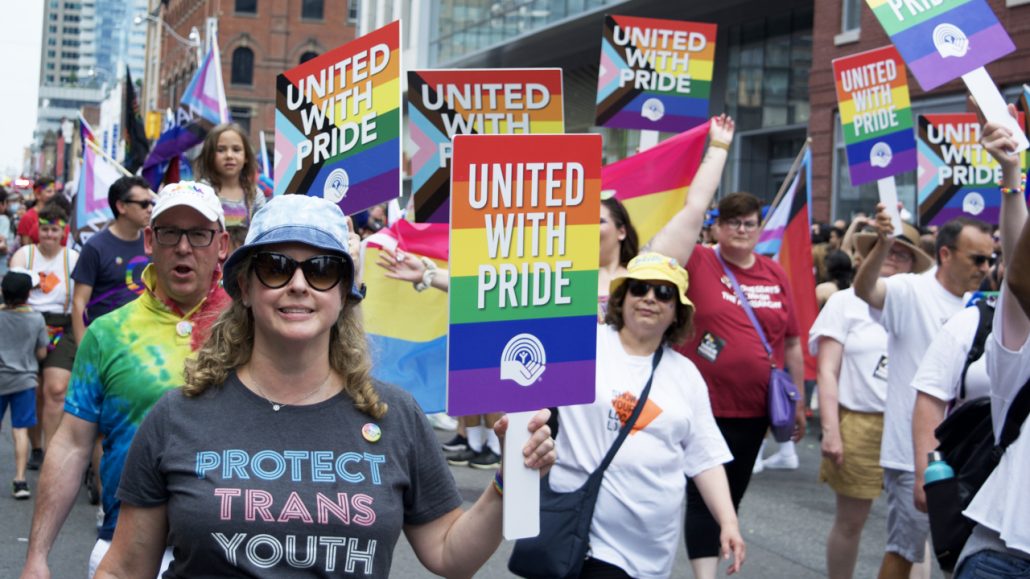 United Way staff and friends marching in the Toronto Pride Parade and holding up signs with the words 'United with Pride.'