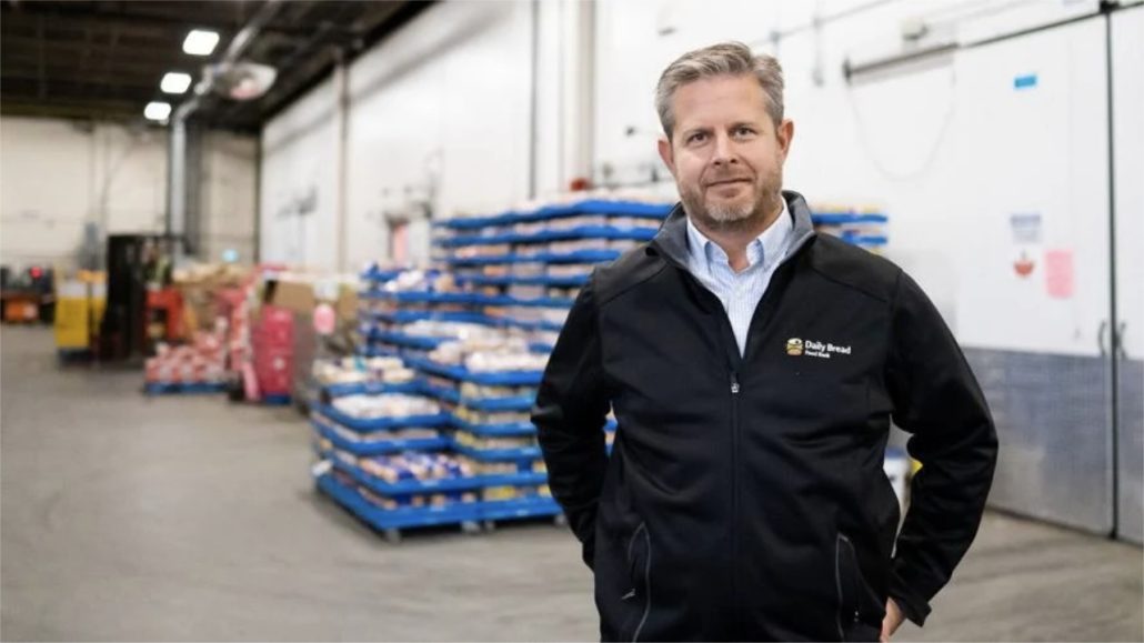 Neil Hetherington, CEO of Daily Bread Foodbank in warehouse surrounded by pallets of food.