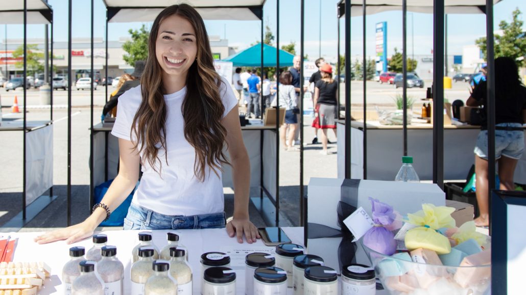 A woman standing behind a table filled with body care products.