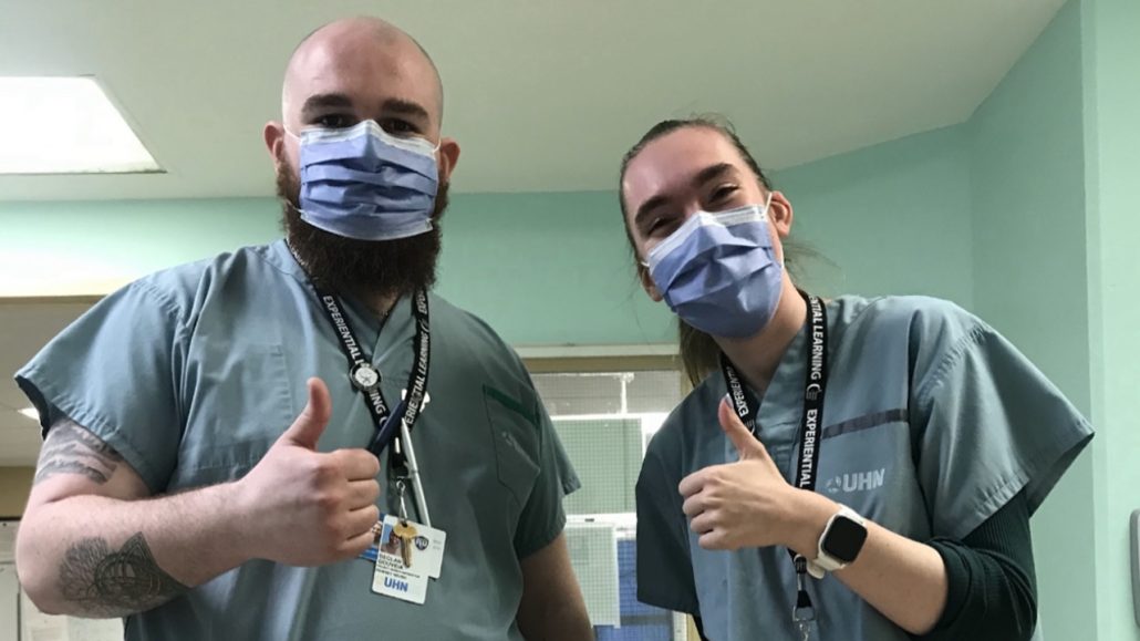 A man and woman wearing scrubs and masks and giving the thumbs up sign.