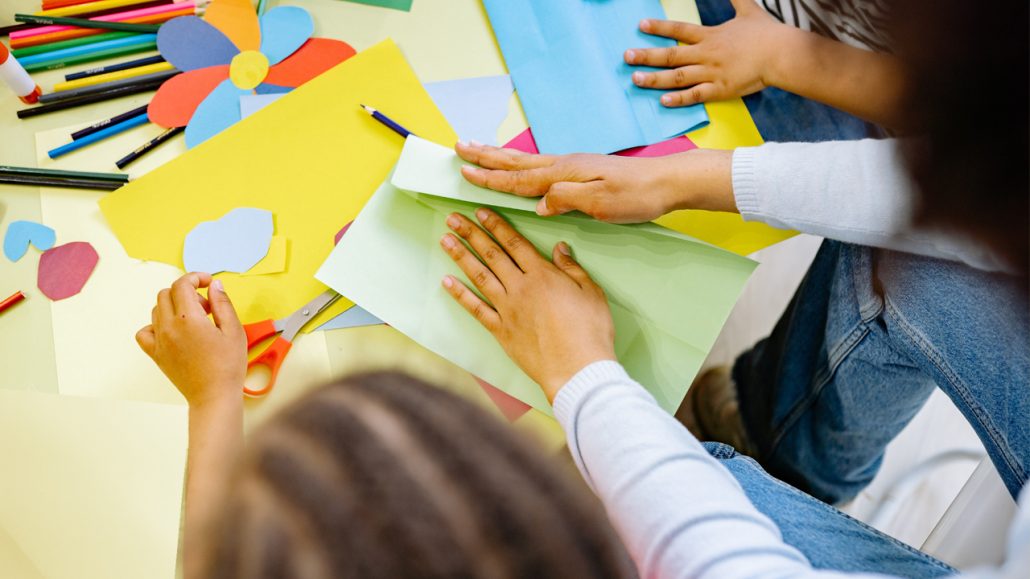 Kids sitting at a table making cards with coloured paper and pencil crayons.