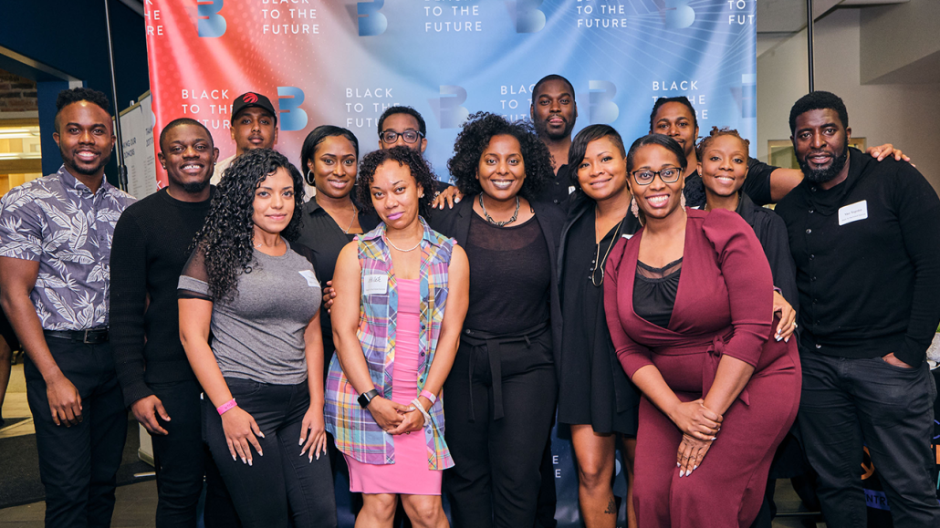 A group of smiling people posing in front of a backdrop with “Black to the Future” written on it.