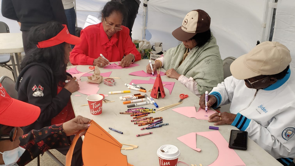 Four adults sitting round a table and crafting with paper, scissors, crayons and marker pens.