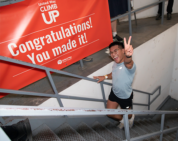 A man smiling and making the peace sign with his hand as he climbs up the last few steps of the CN Tower at United Way’s ClimbUP fundraising event.