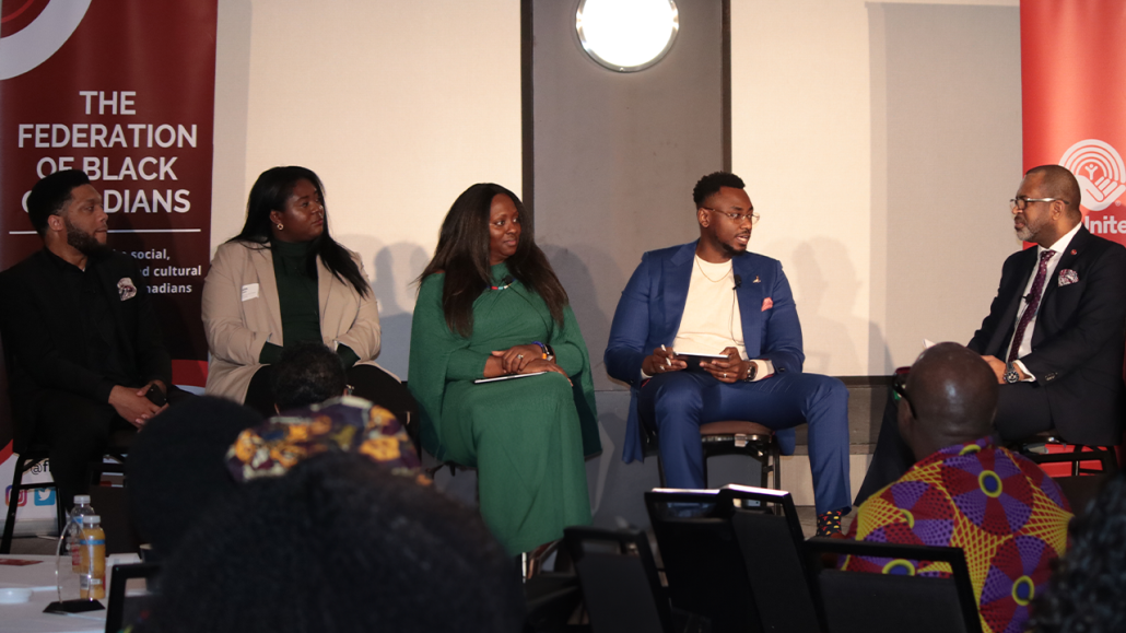 Four panellists and a moderator from the Black Leadership and Recognition Breakfast Event on a stage talking in business casual.