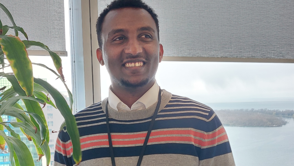 Biruk Tilahun stands in front of a window smiling.