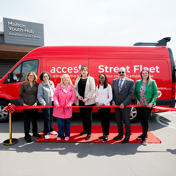 Staff from United Way and United Way-supported ACCES Employment stand behind a ceremonial ribbon to officially launch a mobile employment support van visible behind them. 