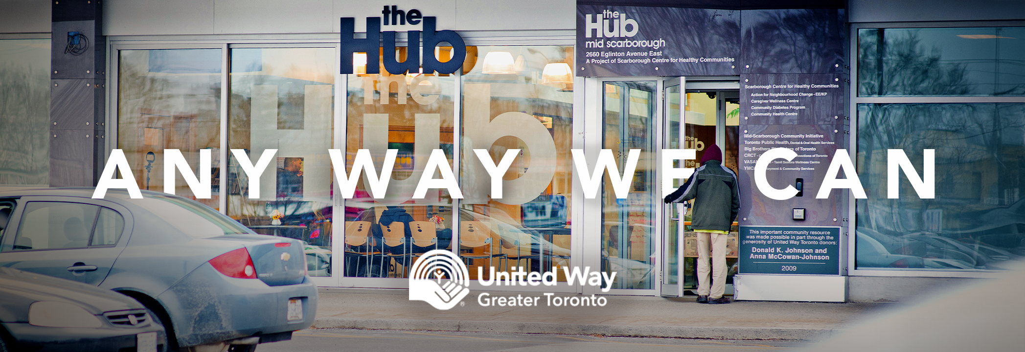 A person walks through the front doors of the United Way-supported Mid-Scarborough Community Hub, with the words ‘Any Way We Can’ and the United Way Greater Toronto logo written on top in white.
