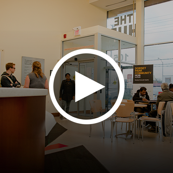 Inside a United Way-funded Community Hub, people sit at tables and stand in conversation. A white arrow in a circle icon is overlaid on the image.
