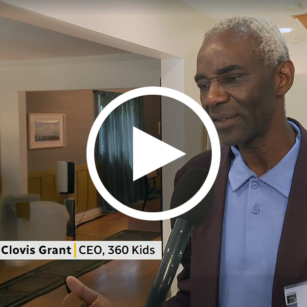 A still of a video of Clovis Grant, CEO of 360°kids and a Black man with gray hair wearing a blue button-up shirt and black jacket, as he speaks into a microphone on the local news.