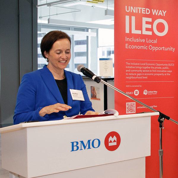 Heather McDonald, President & CEO of United Way Greater Toronto and a white woman with short, brown hair wearing a blue jacket and black shirt. She stands at a white podium with the BMO logo with a sign next to her that says “United Way, ILEO, Inclusive Local Economic Opportunity.”