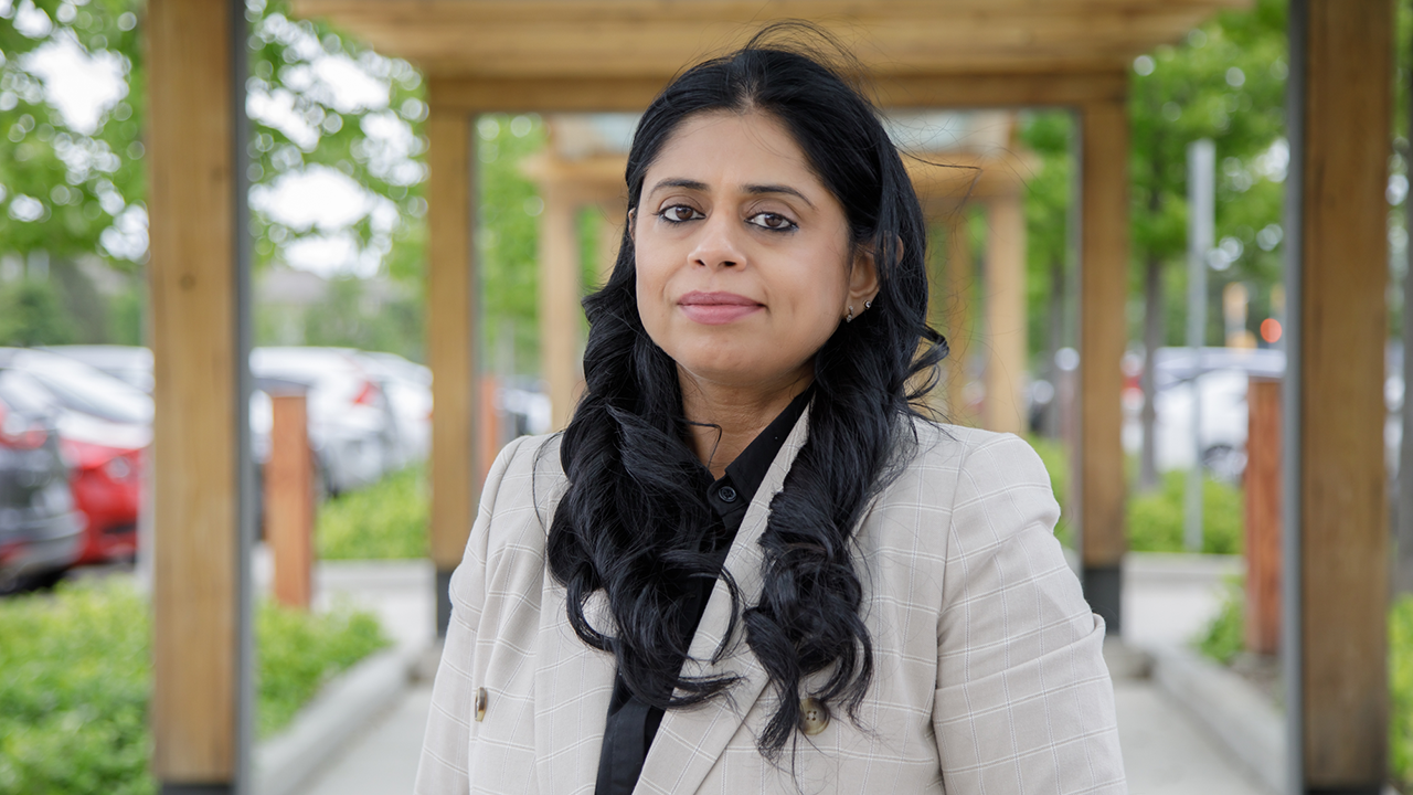 Rakhee stands outside, staring straight at the camera, in a cream coloured suit jacket.