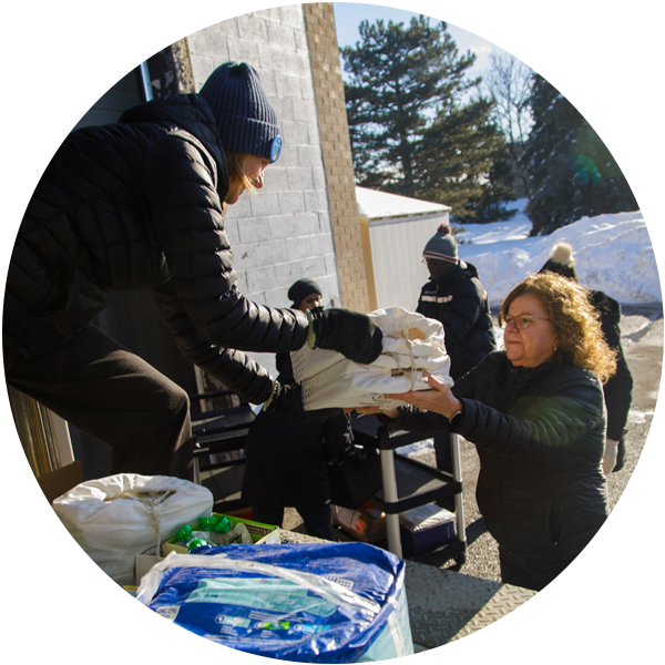 A woman in a truck handing another woman a food hamper at Caledon Community Services’ food bank, The Exchange, on a sunny winter day.