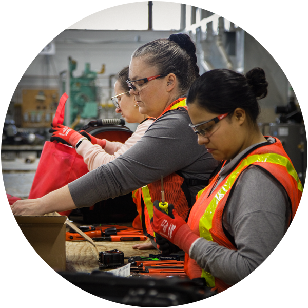 Three women wearing safety vests and goggles work with machinery as part of the Redwood Shelter’s Women in Trades and Technology program. 
