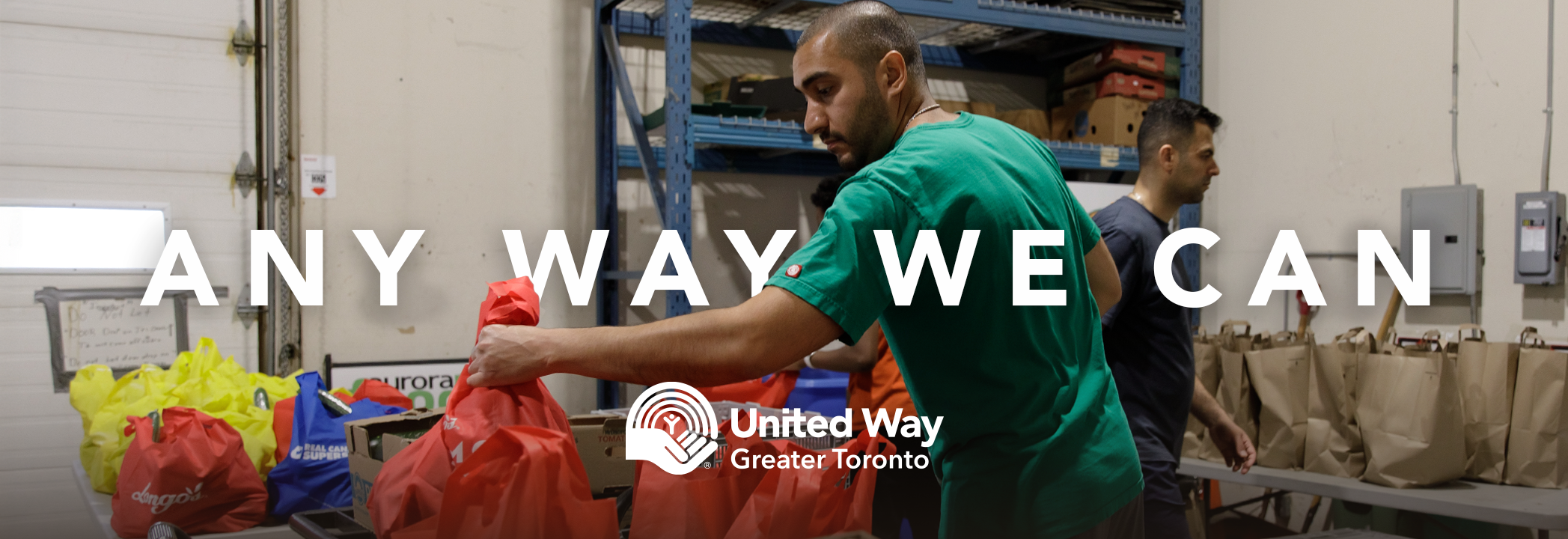 A man wearing a green shirt arranges reusable bags filled with food at a food bank, with the words ‘Any way we can’ and the United Way Greater Toronto logo in white. 
