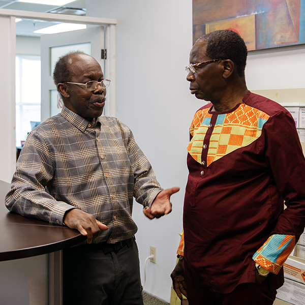 Kwaku, a Black man wearing a plaid shirt, speaks to Boafo, a Black man wearing a red shirt with a colourful design, at African Community Services of Peel.